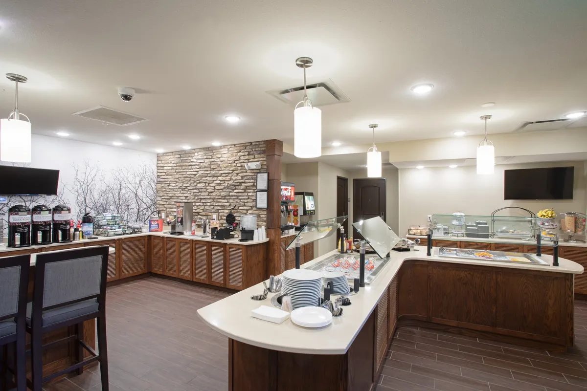 A welcoming breakfast bar area adorned with a coffee station and a stone feature wall. The food display is set up for guests to enjoy breakfast, while comfortable seating invites socializing and relaxation. The warm lighting creates a cheerful morning atmosphere.