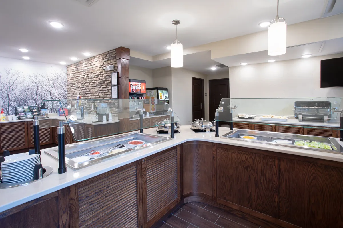 A bright and inviting buffet area with a stone accent wall, stylish hanging light fixtures, and a counter offering various breakfast options. The casual dining space is set up for guests to enjoy meals and interact comfortably.