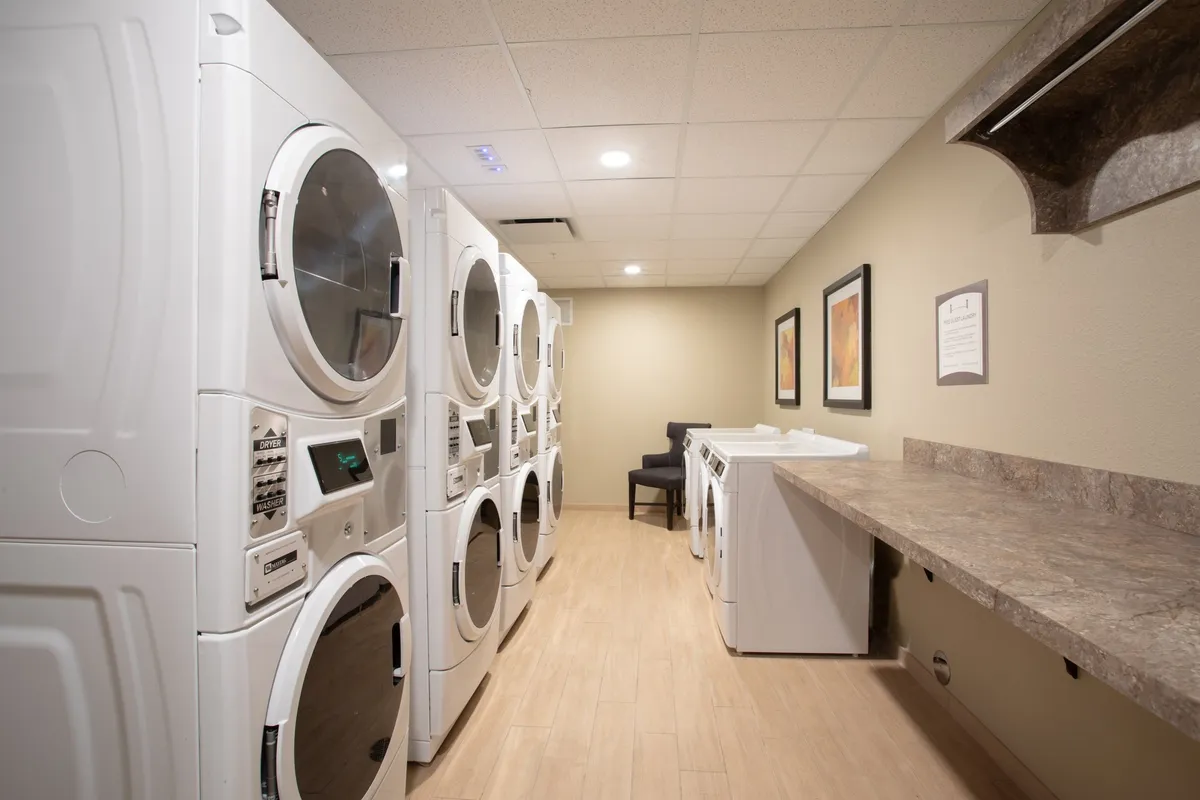A practical laundry room equipped with multiple laundry machines, a countertop for folding, and a small seating area for waiting or reading. The space is clean and organized, emphasizing functionality.