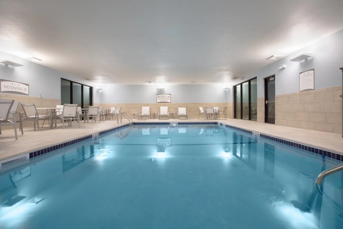 A serene indoor swimming pool area with sparkling blue water, comfortable lounge chairs, and elegant lighting fixtures, creating a tranquil environment for relaxation and socialization.