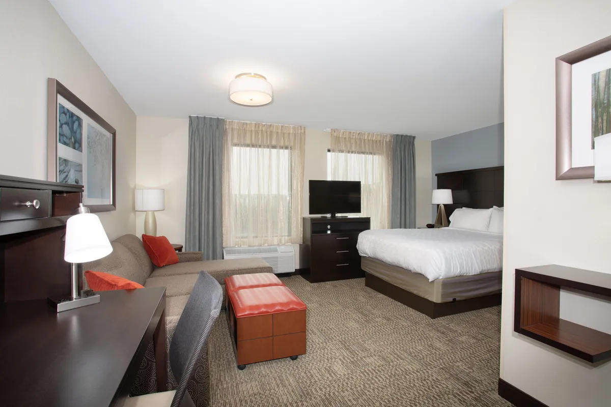 This cozy studio interior features a plush queen bed, a comfy sofa ideal for lounging, a flat-screen TV for movie nights, and soft window curtains that let in natural light—creating a warm, inviting atmosphere perfect for unwinding after exploring Denver.