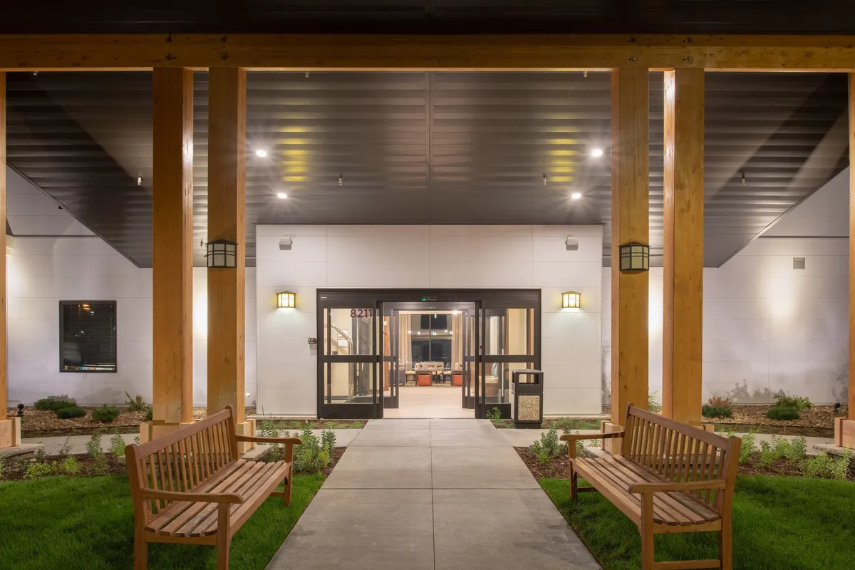 The hotel’s exterior entrance showcasing a well-maintained doorway, benches surrounded by tasteful landscaping, and welcoming lighting fixtures. The area exudes a sense of hospitality from the very first impression.